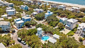 Vue aérienne d’un quartier résidentiel situé sur la côte, avec des maisons, une piscine et une plage en arrière-plan.
