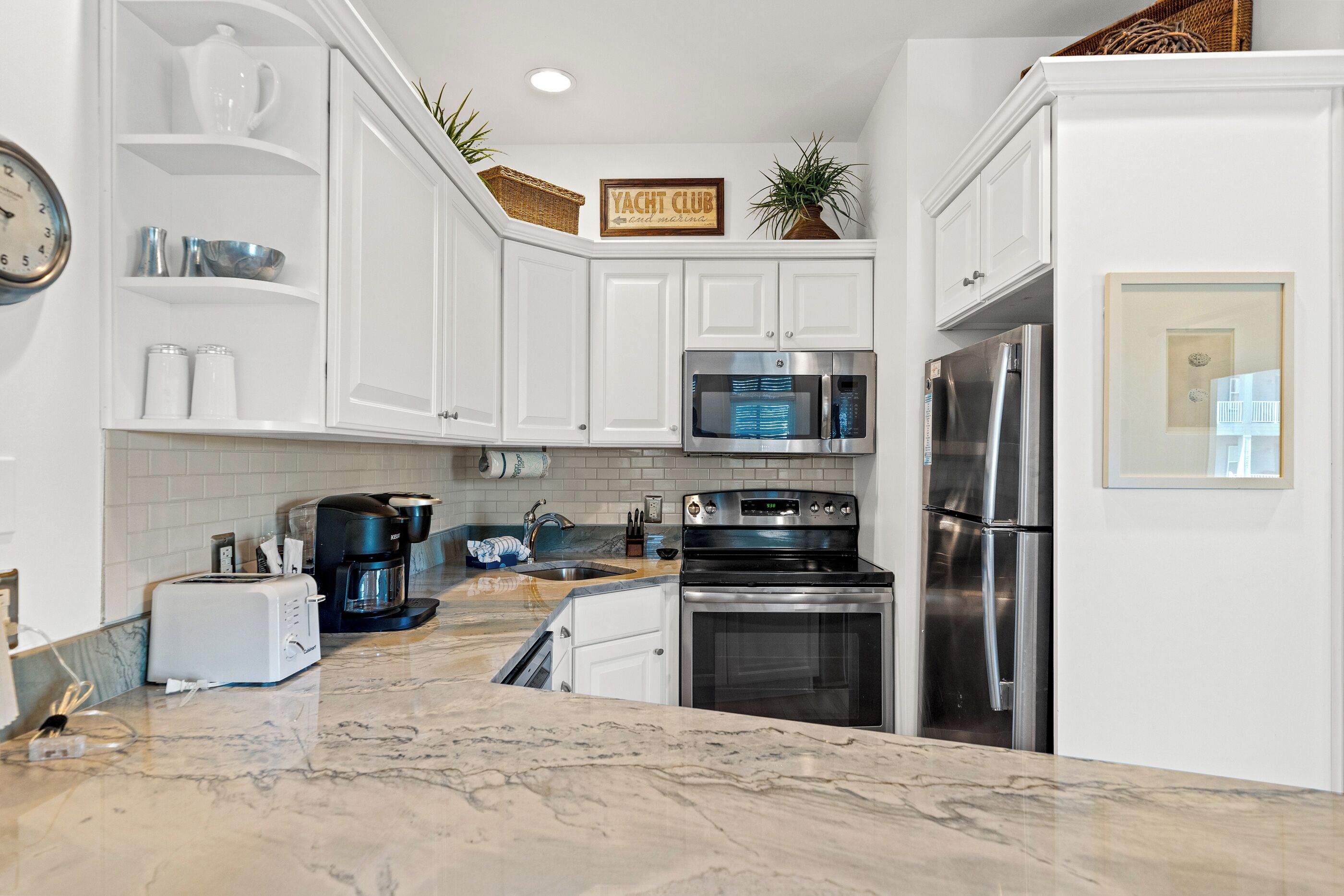 A kitchen with white cabinets, a stainless steel refrigerator, a microwave, a stove, and a coffee maker.