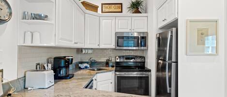 A kitchen with white cabinets, a stainless steel refrigerator, a microwave, a stove, and a coffee maker.