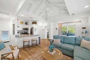A spacious living area with a blue sofa, a round coffee table, and a kitchen with white cabinetry.
