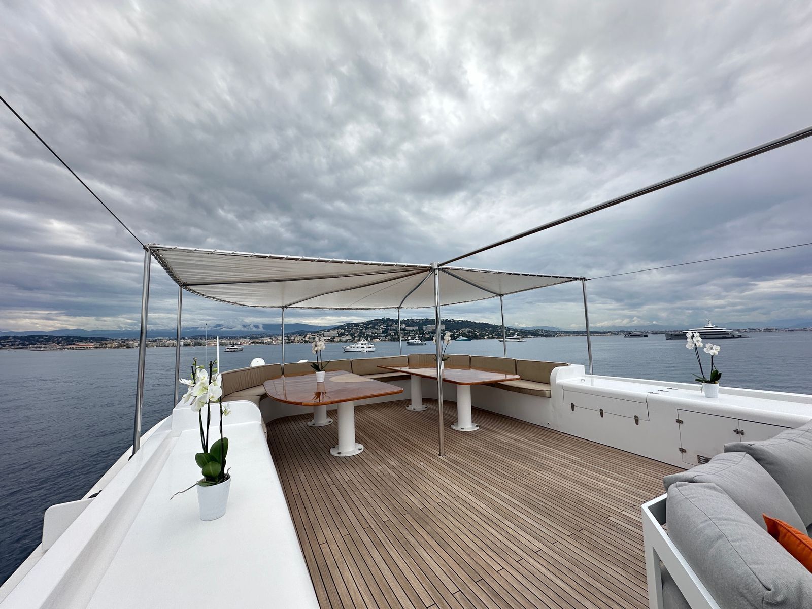 A covered deck with a wooden floor, seating area, and a view of the water and distant land.