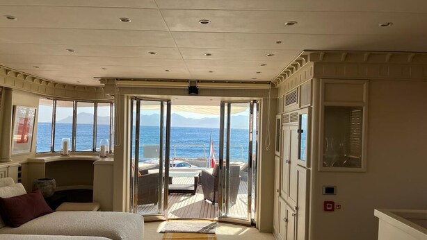 Een kamer met een bed, uitzicht op zee en een deur naar een buitenruimte met een tafel en stoelen.