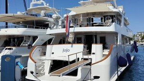 Een grote jacht afgemeerd in een jachthaven, met meerdere dekken en de naam 'Jojo' duidelijk zichtbaar.