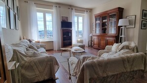 A living room with a sofa set, a cabinet, a television, and a view of the city through large windows.