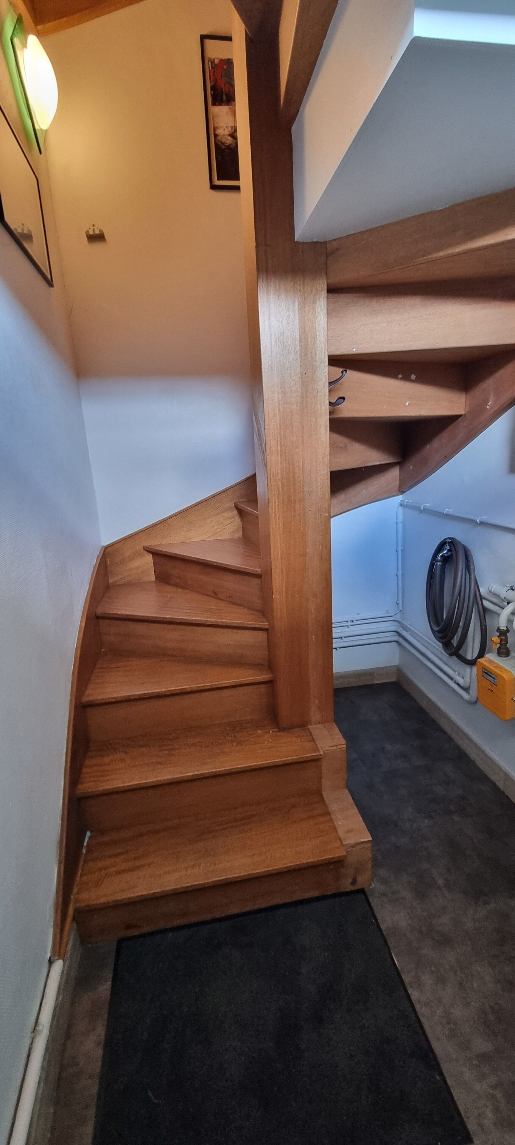A wooden staircase with a black mat at the bottom, a light fixture on the wall, and a framed picture above it.