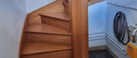 A wooden staircase with a black mat at the bottom, a light fixture on the wall, and a framed picture above it.