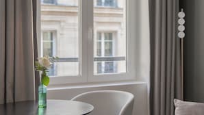 A modern room with a round table, a white chair, a sofa, and a window with curtains. - Hotel Leev Victoire & Spa (Paris)