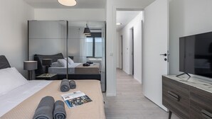 A modern hotel room with a large bed, a TV, a mirror, and a walk-in closet.
