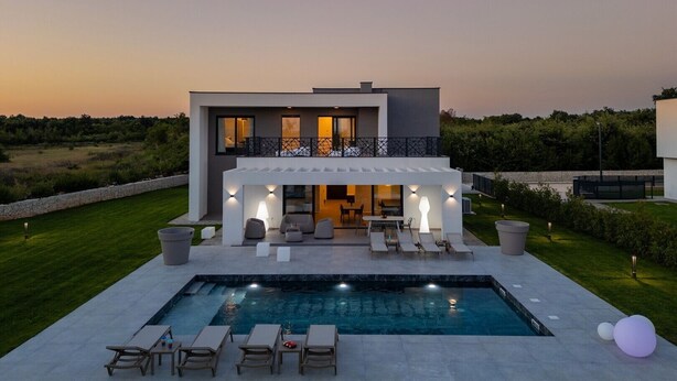 A modern two-story house with a pool, outdoor seating, and a well-maintained lawn.