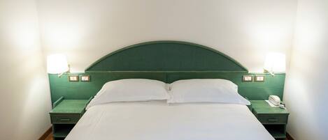 A neatly made bed with white linens in a hotel room.