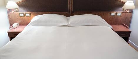 Una cama doble con cabecera de madera, dos mesitas de noche con lámparas y un teléfono en una de ellas.