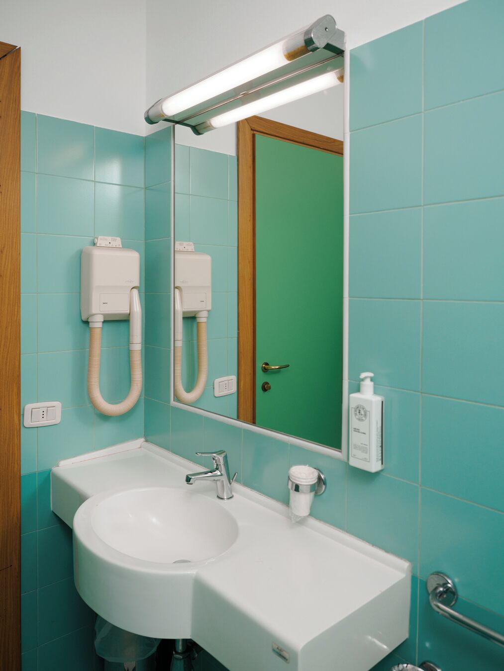A bathroom with a white sink, a mirror, and a green door.