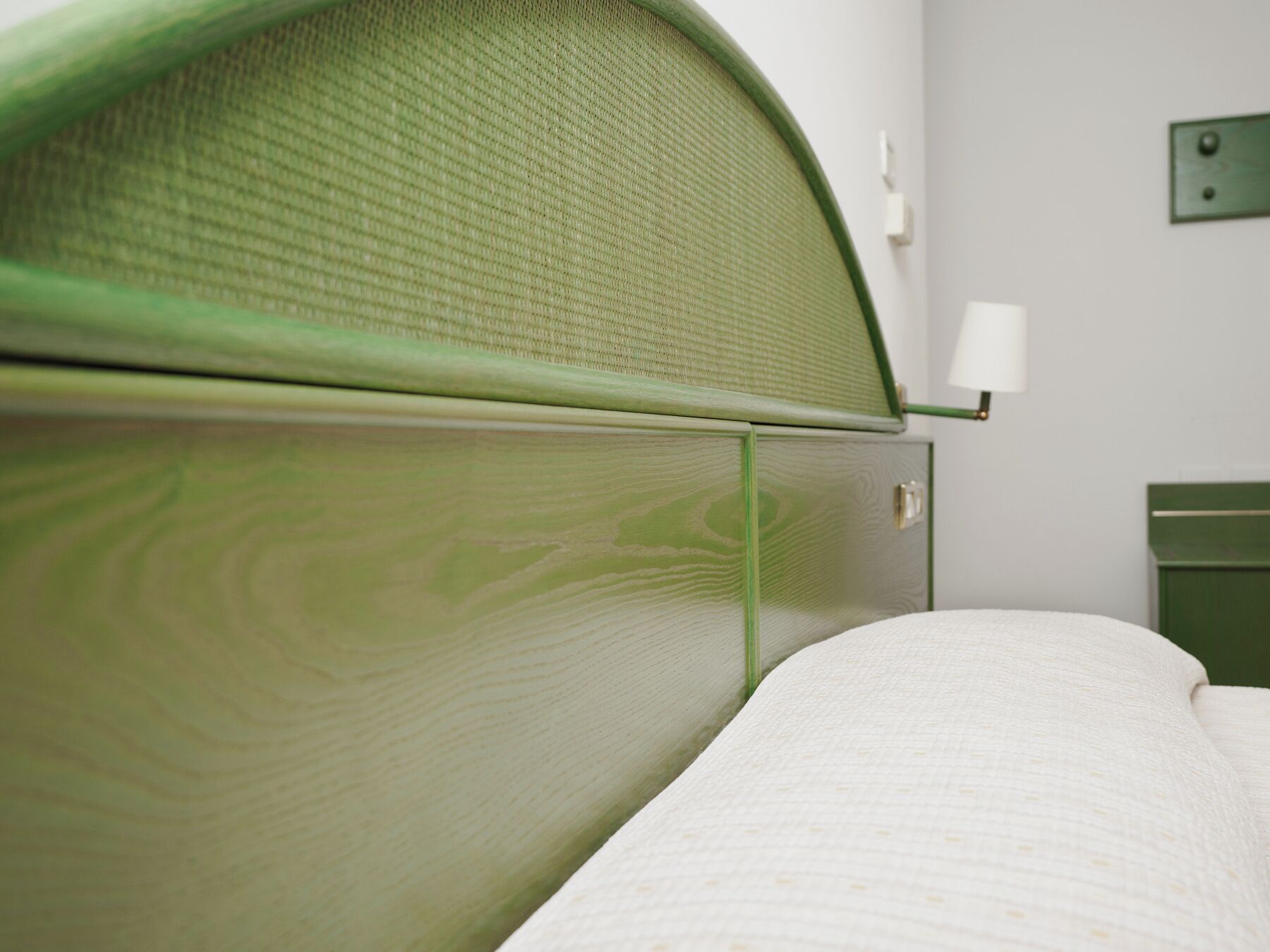 A room with a green headboard, a white bedspread, and a small bedside table with a lamp.
