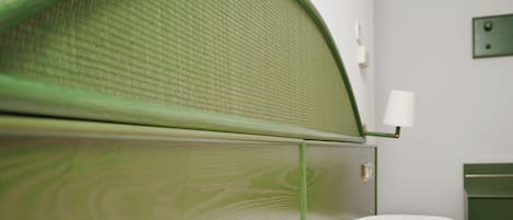 Una habitación con cabecera verde, edredón blanco y una mesita de noche con lámpara.