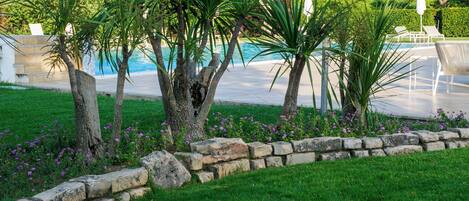 A landscaped garden with a pool, stone border, and lounge chairs.