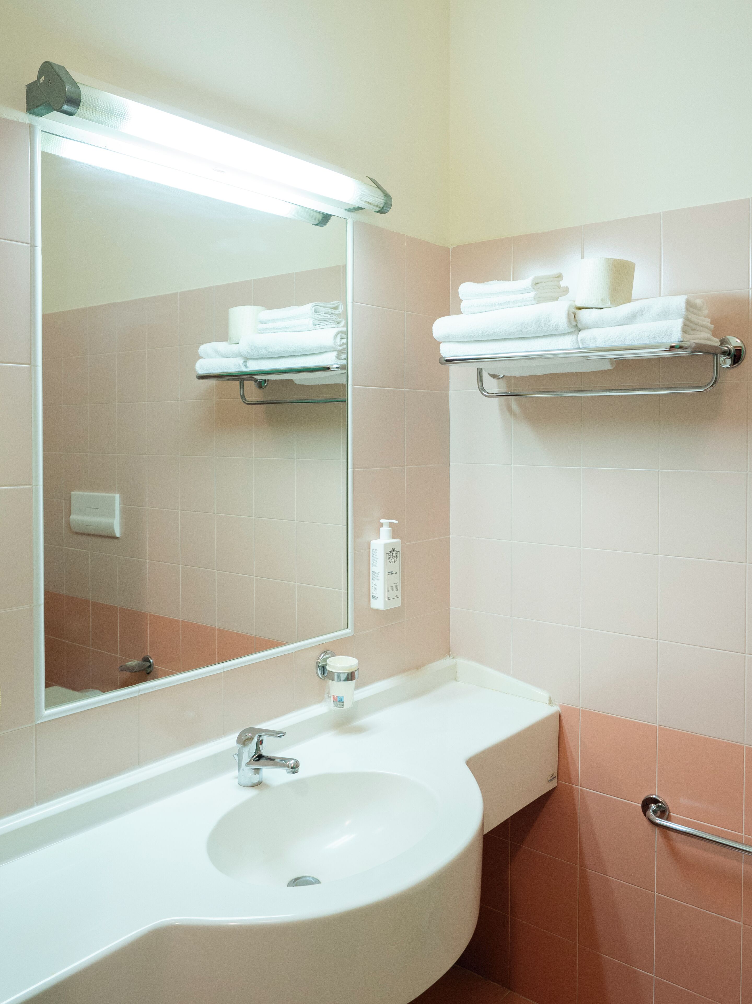 Un baño con lavamanos blanco, espejo y toalleros.