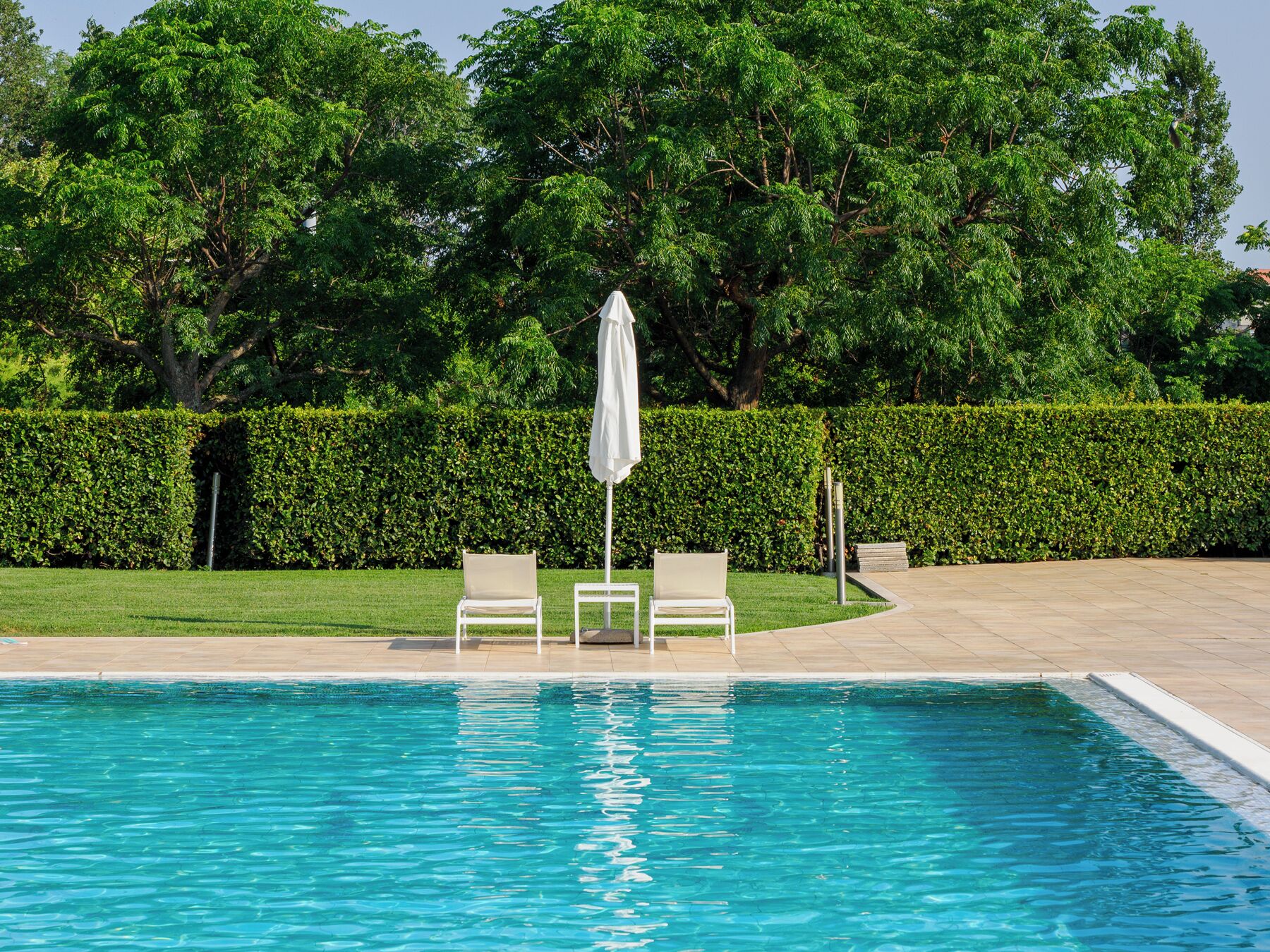 Una piscina con dos sillas reclinables blancas y una sombrilla blanca.