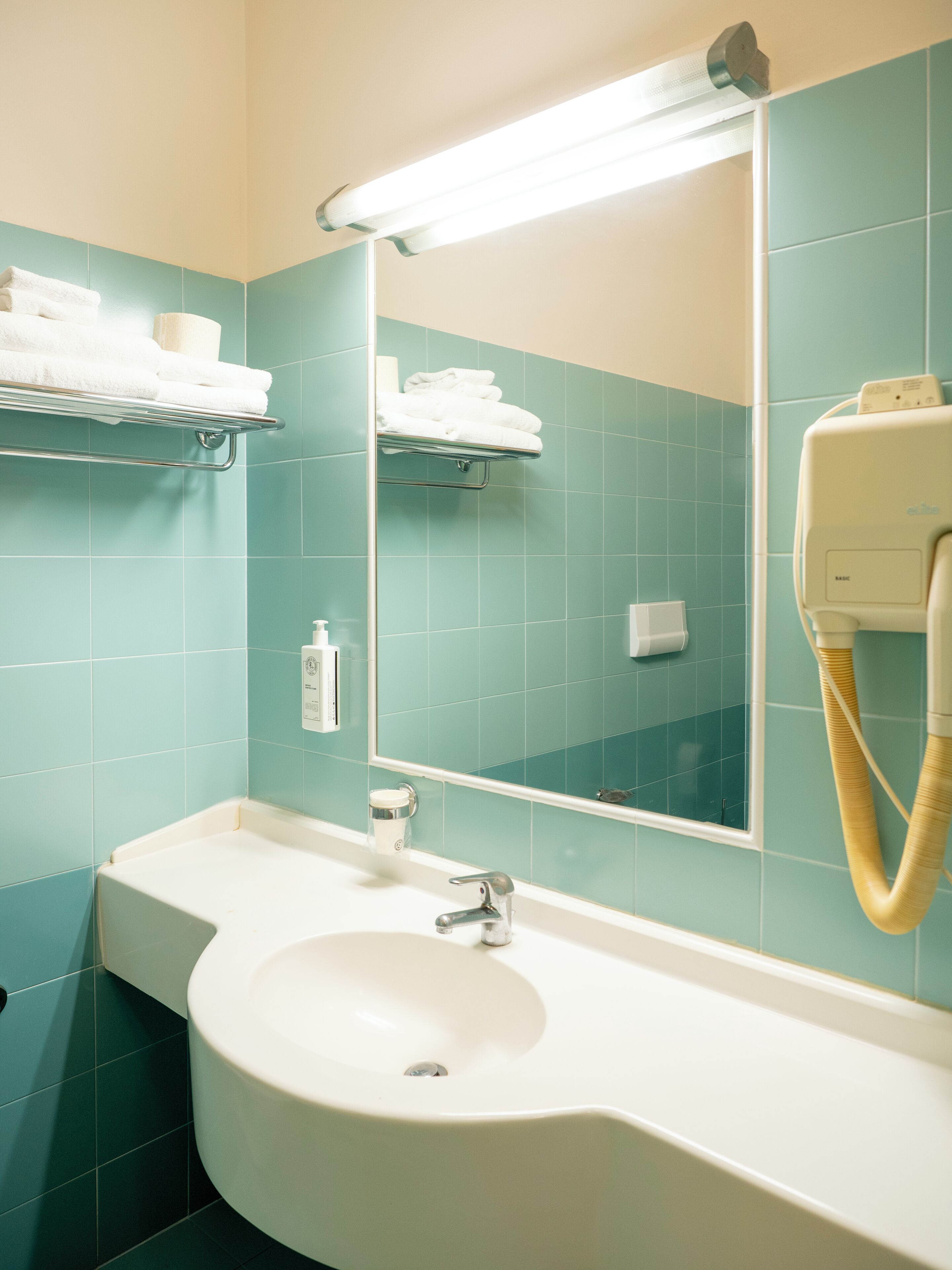 Un bagno con piastrelle color acquamarina, un lavandino bianco, uno specchio e un portasciugamani.
