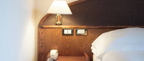 A wooden bedside table with a telephone, a lamp, and a switch.
