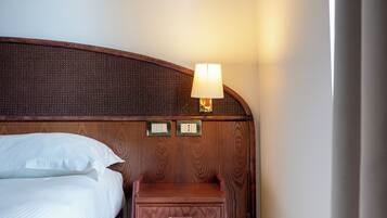 Een hotelkamer met een houten hoofdeinde, een nachtkastje met een lamp en een bed met witte lakens.