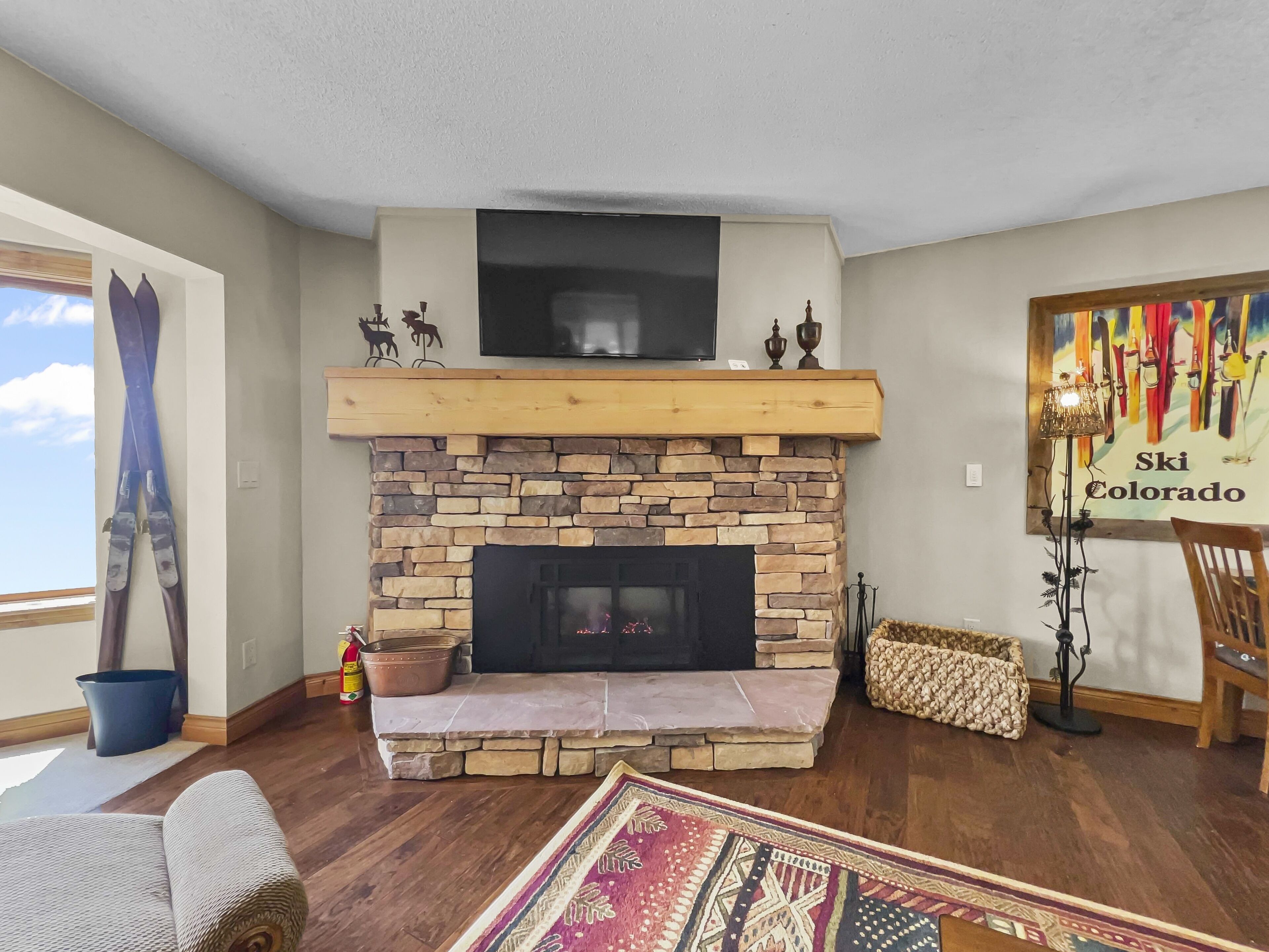 A living room with a stone fireplace, a mounted television, and a ski-themed poster.