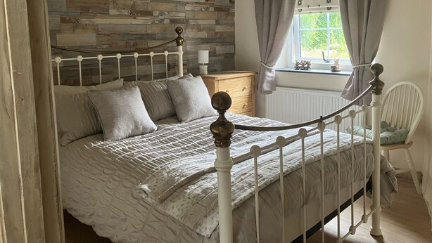 A bedroom with a wooden headboard, a bed with a white metal frame, a nightstand, a chair, and a window with curtains. - Annie's Cottage, Wellington
Stunning Cottage in lake District National Park (Seascale)