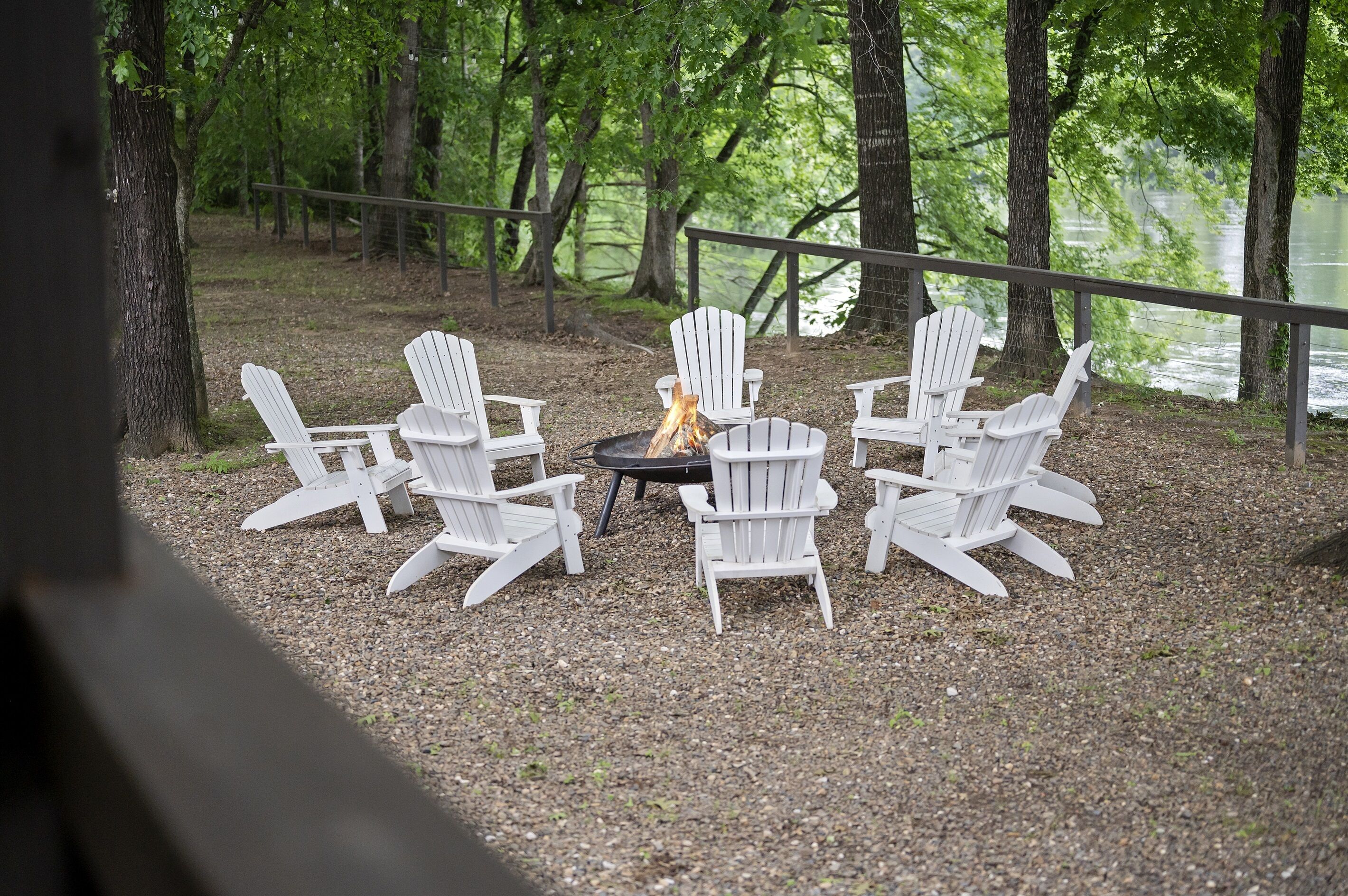 Een terras met Adirondack-stoelen rond een vuurkorf, met uitzicht op een meer.
