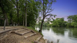 A riverside walkway with steps leading to a viewing area, surrounded by trees and a calm river.