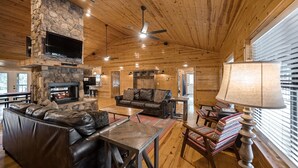 A cozy cabin interior with a stone fireplace, leather sofa, and wooden furniture.