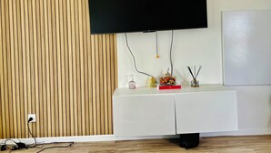 Una sala moderna con un televisor de pantalla plana montado, un mueble blanco para equipo con objetos decorativos y un panel de pared de madera.