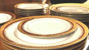 Una pila de platos blancos con detalles dorados y un diseño decorativo, sobre una superficie de madera.