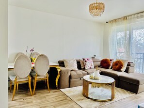 En moderne stue med spiseplads, med en sofa, et rundt sofabord og en lysekrone.