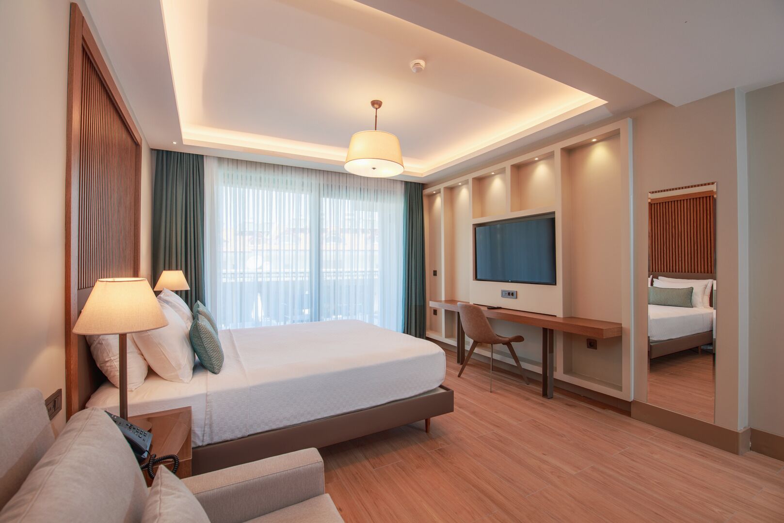 A modern hotel room with a large bed, a desk, a television, and a mirror.