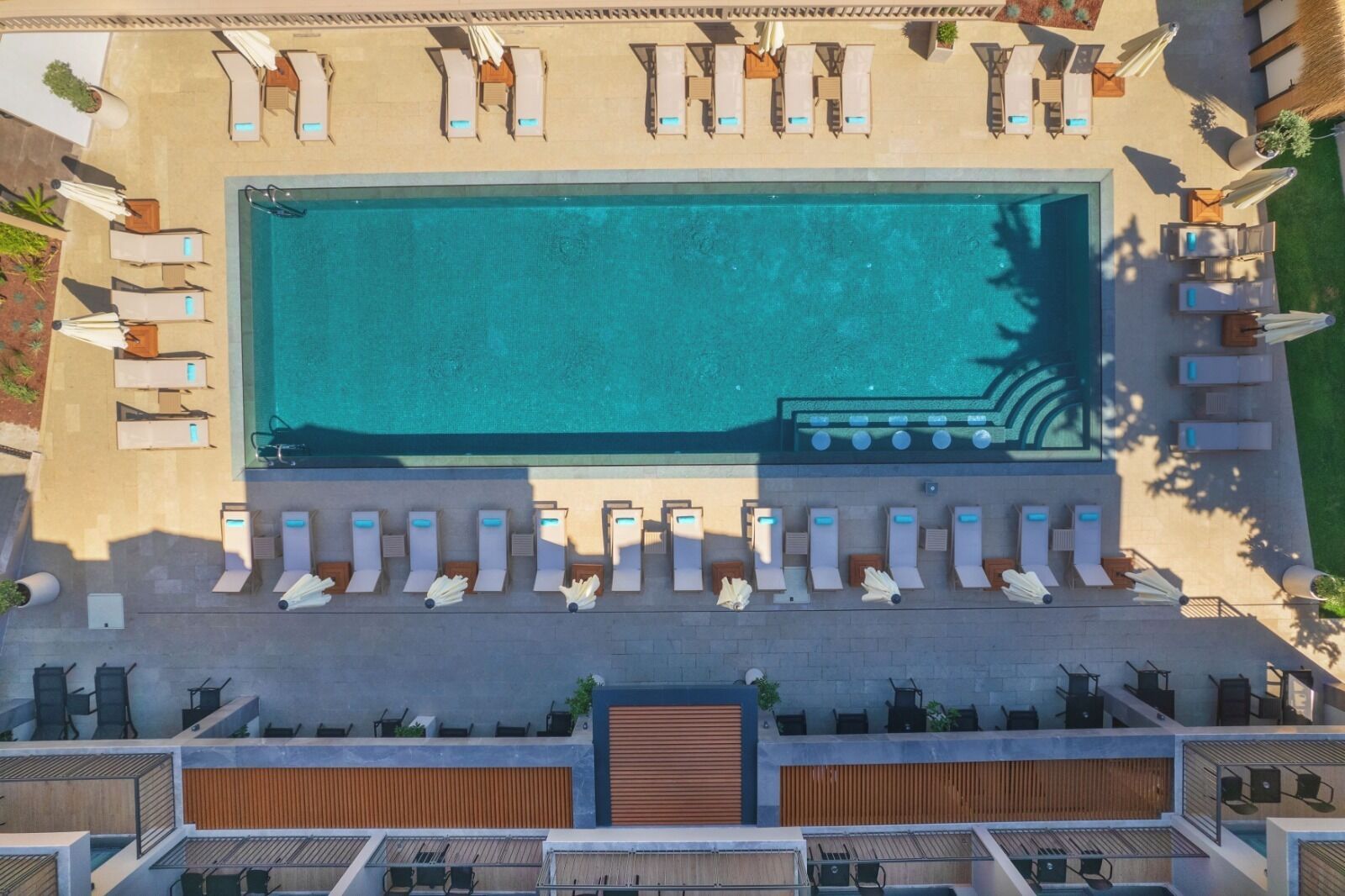 An aerial view of a swimming pool area with multiple sun loungers and a poolside bar.