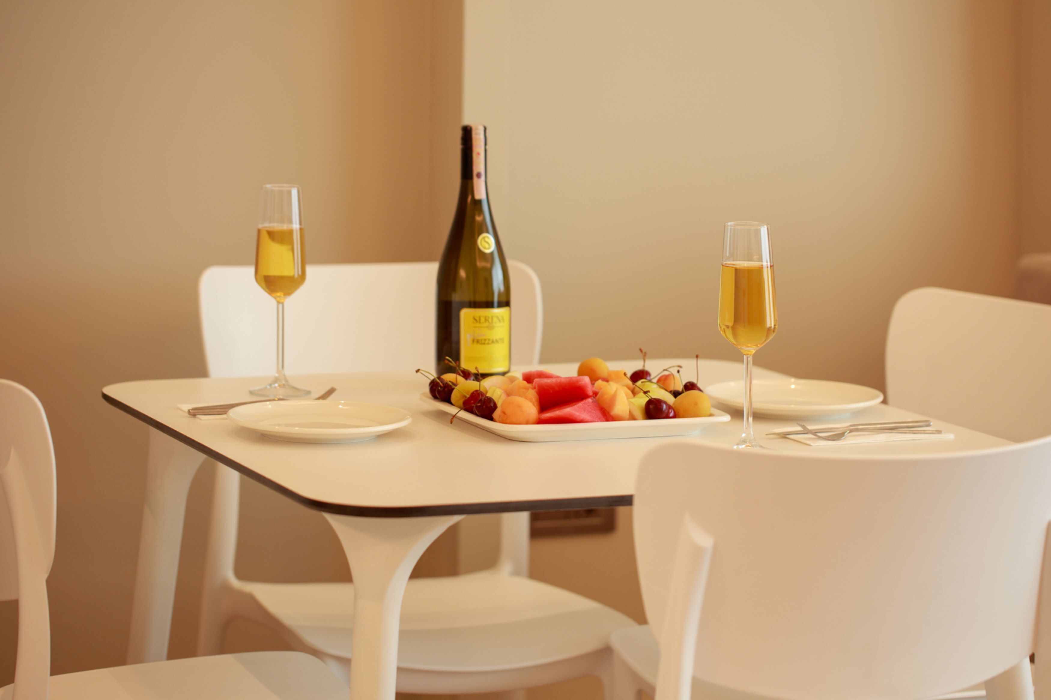 A dining table with a bottle of wine, two glasses of wine, and a fruit platter.