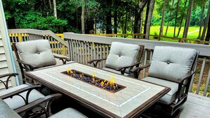 A covered outdoor patio with a rectangular table and four cushioned chairs. - Cozy Carolina Trace 3BR w/ Relaxing Golf Course Views - Deck & Fire Table (Sanford)