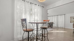A dining area with a round table and four chairs, a chandelier, and sheer curtains. - Cozy Carolina Trace 3BR w/ Relaxing Golf Course Views - Deck & Fire Table (Sanford)