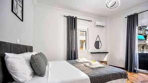 Moderni hotellihuone, jossa on sänky, yöpöytä, tuoli ja näkymä ulkoalueelle.