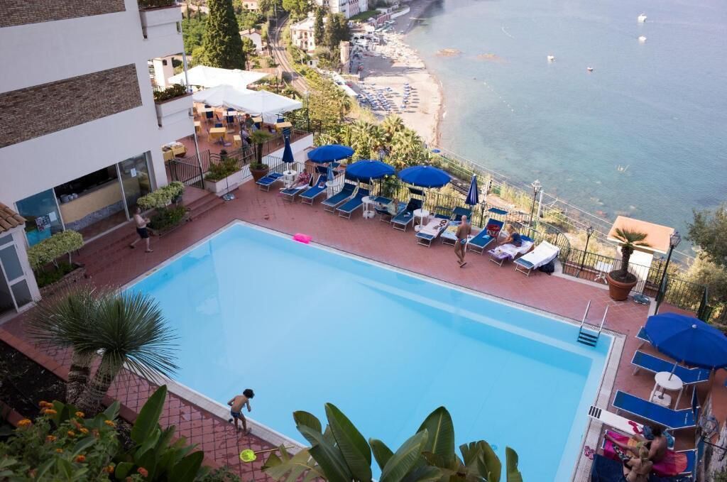 A pool area with lounge chairs and umbrellas, overlooking a beach and the sea.