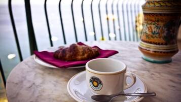A table with a cup and saucer, a spoon, and a croissant on a plate.