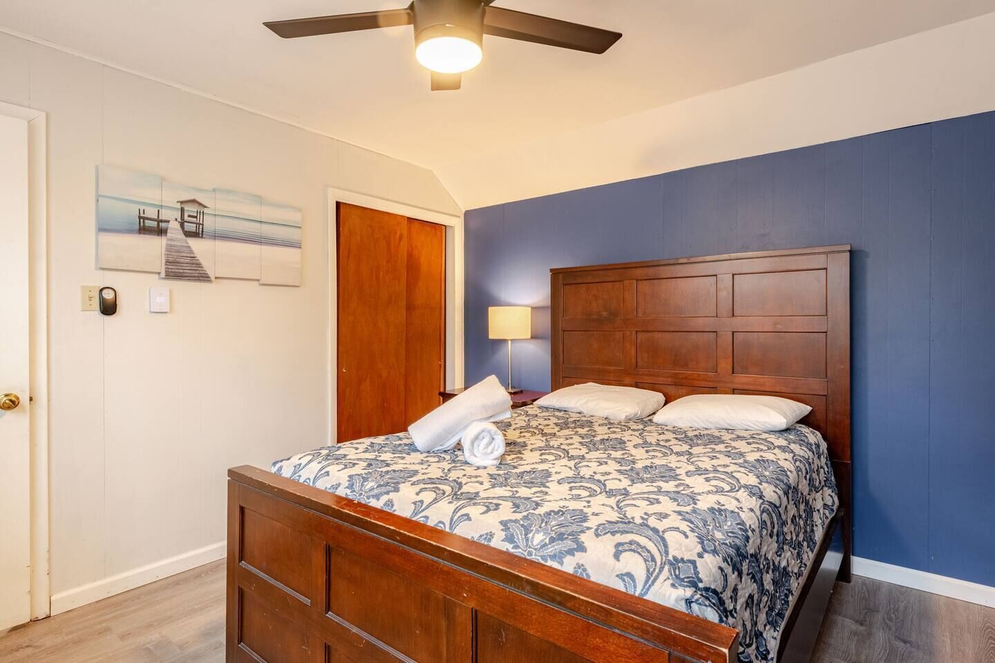 A bedroom with a wooden bed, a ceiling fan, a nightstand, and a painting on the wall.
