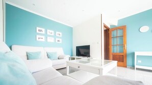 A modern living room with a white sofa, a glass coffee table, and a television.