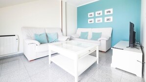 A modern living room with a white sofa, a glass coffee table, and a white TV stand.