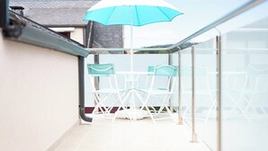 A balcony with a glass railing, a white table, and two chairs.