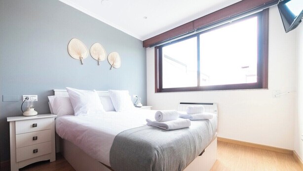 A modern bedroom with a large bed, bedside tables, and a window with blinds.