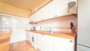 Uma cozinha com armários brancos, bancada de madeira, máquina de lavar, pia e porta-facas.