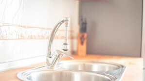 Uma pia de aço inoxidável com uma torneira moderna, bancada de madeira e uma janela ao fundo.
