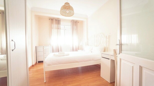 Quarto com cama, mesa de cabeceira e luminária suspensa.