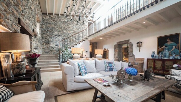 A spacious living area with a stone wall, a white sofa with colorful cushions, a wooden coffee table, and a staircase leading to an upper level. - Villa Los Magnolios "Paderne" (Paderne)