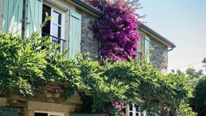 A stone building with green shutters, outdoor seating, and a garden with purple flowers. - Villa Los Magnolios "Paderne" (Paderne)